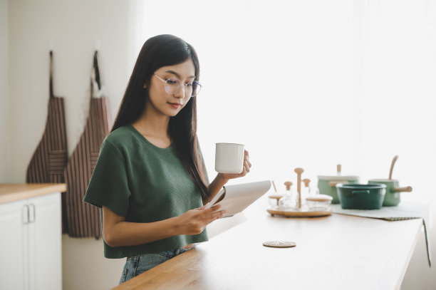 快乐的年轻亚洲女人在家里的厨房戴眼镜。女专心读书注意做饭图片下载