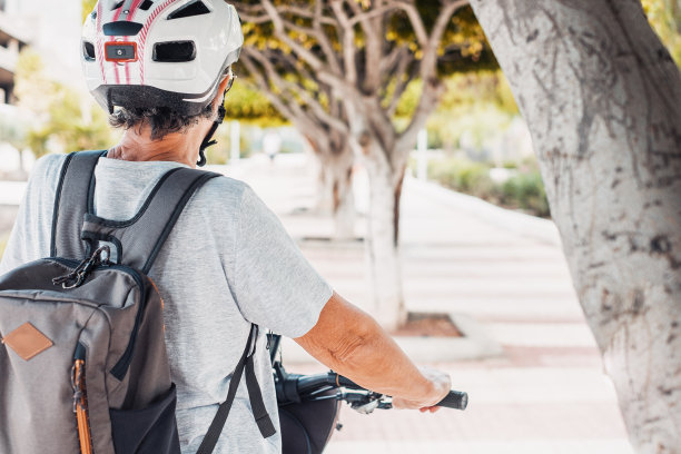 城市公园骑自行车的老年妇女，戴着头盔，背着背包，骑着电动自行车。健康的生活方式和可持续的出行理念图片下载