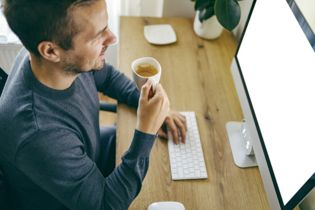 一位自由职业者坐在现代化的家庭办公室里，一边喝着咖啡，一边在键盘上打字，对着屏幕微笑。图片下载