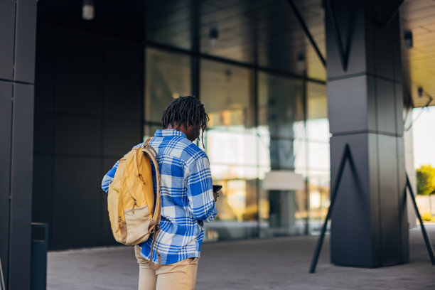 商务男子在格子衬衫与背包去工作和使用手机的背影图片下载