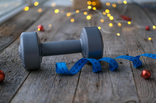 圣诞节后的运动和减肥的概念。哑铃和卷尺，背景是木制的圣诞彩灯。图片下载