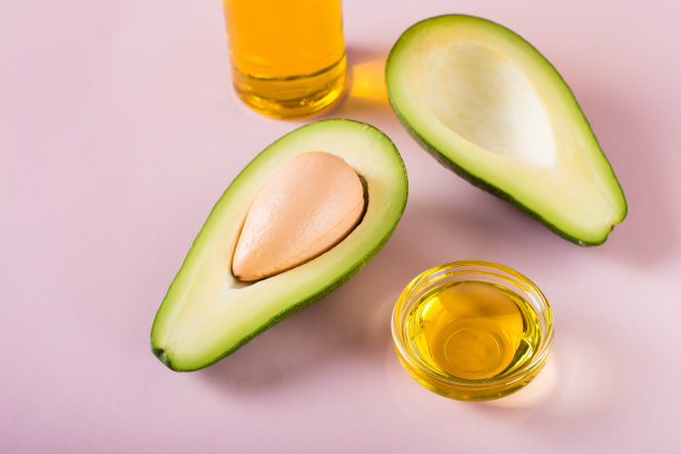 成熟的牛油果和牛油果油在碗和瓶在粉红色的背景。家庭美容。图片下载