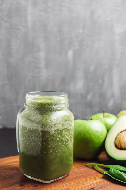 绿色冰沙饮料混合在玻璃罐中，鳄梨，菠菜叶和苹果在木板上图片下载