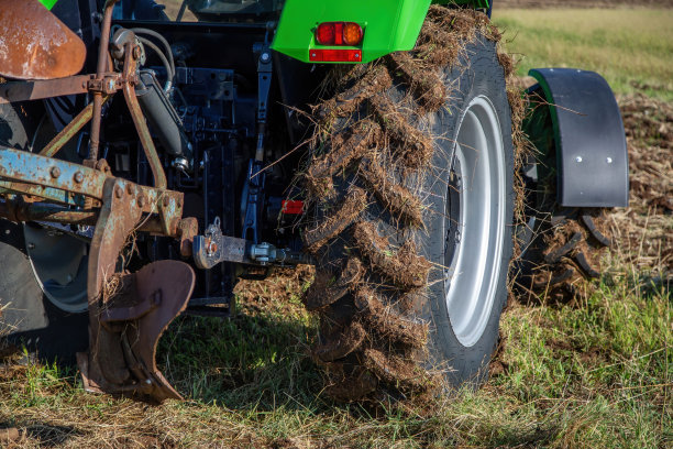 带犁的拖拉机，近距离车轮被泥土覆盖，未耕种的农场背景。农业图片下载