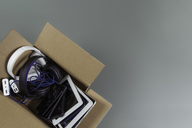 纸箱里装满了旧电脑、平板电脑、智能手机、可回收的电子产品，背景是灰色的。捐赠，电子垃圾，电子垃圾再利用，翻新，回收概念图片下载