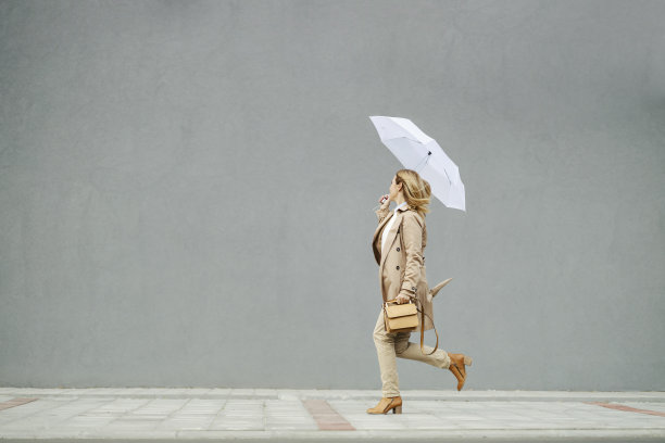在阴雨的天气里，一位穿着休闲服装的女商人打着伞在跑步。图片下载
