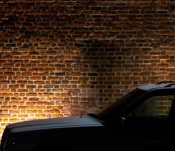 一辆白色汽车在夜间停在一堵发光的红砖墙旁。图片下载