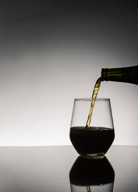 啤酒从酒瓶中倒进玻璃杯，酒瓶映在桌子上的深色背景上图片下载