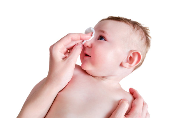 母亲用化妆棉擦拭快乐婴儿的脸，隔离在白色背景上。妈妈在沙发上抱着六到七个月大的微笑幼儿，注意卫生图片下载