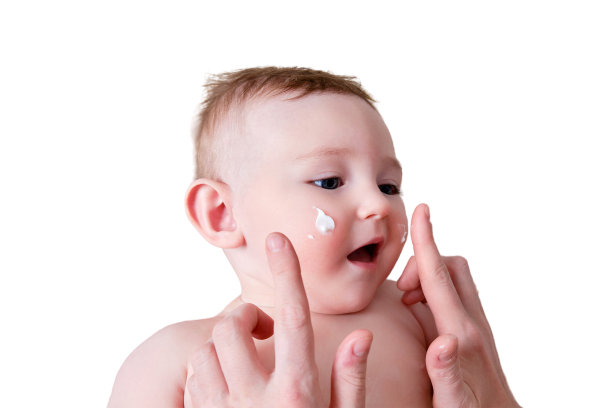 母亲的手正在给一个快乐的婴儿涂抹奶油，婴儿孤立在白色背景上。妈妈在沙发上给六到七个月大的孩子按摩图片下载