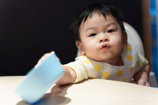 可爱的年轻亚洲婴儿男孩玩食物碗和勺子时，吃饭在桌子上。亚洲家庭婴儿家庭生活理念。图片下载