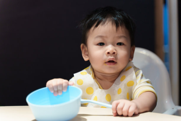 可爱的年轻亚洲婴儿男孩玩食物碗和勺子时，吃饭在桌子上。亚洲家庭婴儿家庭生活理念。图片下载