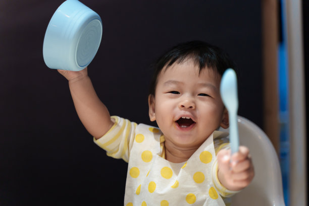 可爱的年轻亚洲婴儿男孩玩食物碗和勺子时，吃饭在桌子上。亚洲家庭婴儿家庭生活理念。图片下载