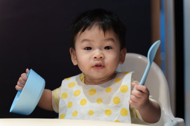 可爱的年轻亚洲婴儿男孩玩食物碗和勺子时，吃饭在桌子上。亚洲家庭婴儿家庭生活理念。图片下载