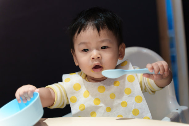 可爱的年轻亚洲婴儿男孩玩食物碗和勺子时，吃饭在桌子上。亚洲家庭婴儿家庭生活理念。图片下载