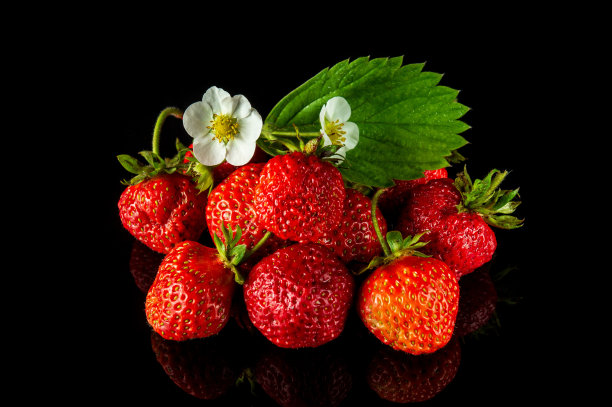 成熟的红色草莓，黑色背景上有叶子和花朵。夏日甜蜜饮食，健康维他命包图片下载
