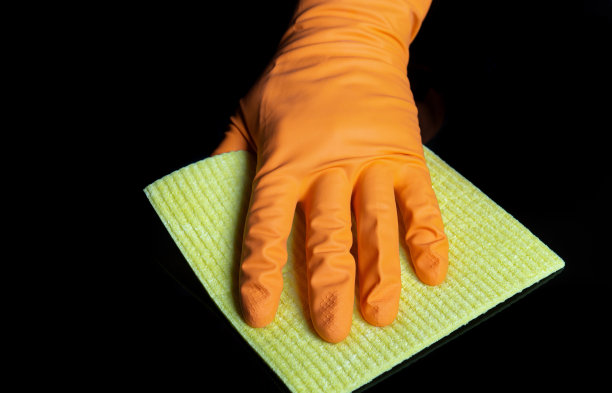 戴着手套的手用黄色餐巾擦黑桌子。家庭清洁过程的特写镜头。冠状病毒期间的医疗保健和消毒概念图片下载