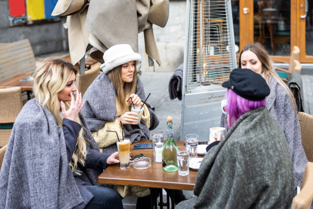 四个穿着暖和衣服的年轻女子坐在当地的咖啡馆里。图片下载