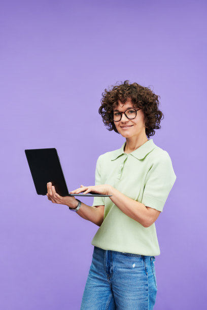 年轻的现代女性在牛仔裤和衬衫使用笔记本电脑，看着相机图片下载