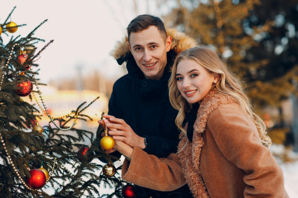 年轻的成年夫妇装饰圣诞树在冬季森林。新年松假日派对庆祝概念。图片下载