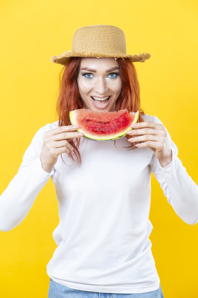 一个可爱的白人漂亮的年轻女子在草帽与多汁西瓜的颜色背景。图片下载