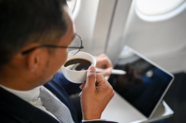 成功的亚洲商人在飞机上边喝咖啡边用平板电脑图片下载