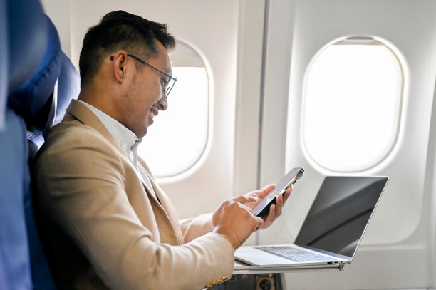侧视图，精明的亚洲商人坐在商务舱靠窗的座位上使用智能手机图片下载