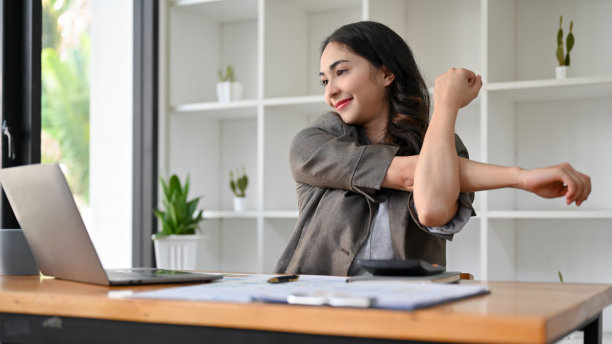 快乐的亚洲女商人在她的办公桌上工作时伸展她的手臂。图片下载