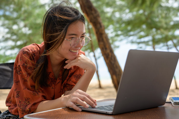 快乐的女性自由职业者坐在舒适的室内舒适的床上，在现代笔记本电脑上远程工作图片下载