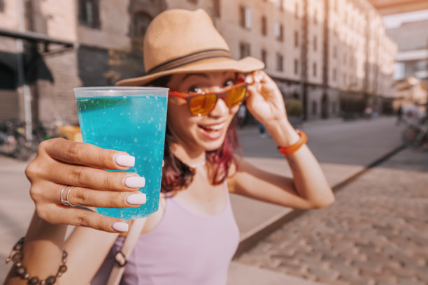 在城市街道喝蓝色苏打鸡尾酒的女孩。酒精和柠檬水饮料图片下载