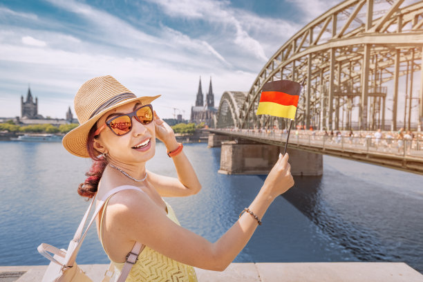 快乐的女孩在莱茵河大桥和科隆大教堂前举着德国国旗。旅游地标和传统节日图片下载