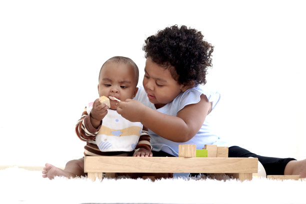 非裔美国卷发女孩试图用勺子喂她的小妹妹，婴儿吃健康的自制婴儿食品，女儿帮助母亲照顾婴儿孩子，童年婴儿护理理念图片下载