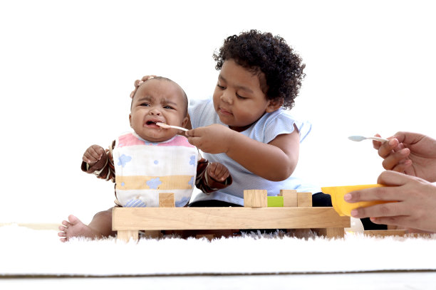 非裔美国卷发女孩试图用勺子喂她的小妹妹，婴儿吃健康的自制婴儿食品，女儿帮助母亲照顾婴儿孩子，童年婴儿护理理念图片下载