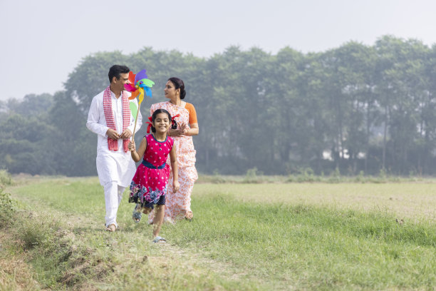 快乐的父母带着可爱的小女孩无忧无虑地奔跑，玩着彩色的针轮。图片下载