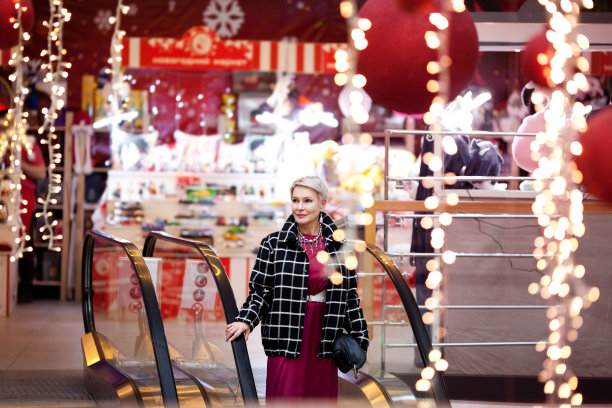 美丽的成熟女子站在购物中心的自动扶梯上，背景是新年或圣诞装饰图片下载