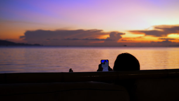 沙滩上拿着手机的女人躺在社交网络上，沉迷于互联网，没有注意到海上美丽的日落。网瘾和海滩度假的虚拟生活图片下载