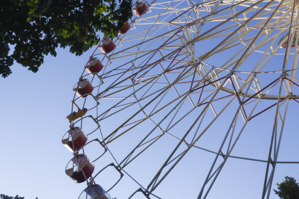 游乐园里的大摩天轮，红色和黄色的小木屋在蓝天的背景下。游乐园里的树图片下载