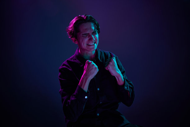年轻男子的肖像在休闲黑色衬衫孤立的渐变深紫色背景在霓虹灯。又高兴又兴奋。人类情感的概念，面部表情。图片下载