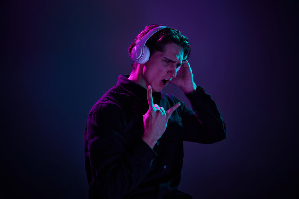 在霓虹灯下，穿着休闲黑色衬衫的年轻人戴着耳机，在渐变色的深紫色背景上隔离。摇滚音乐。人类情感的概念，面部表情。图片下载