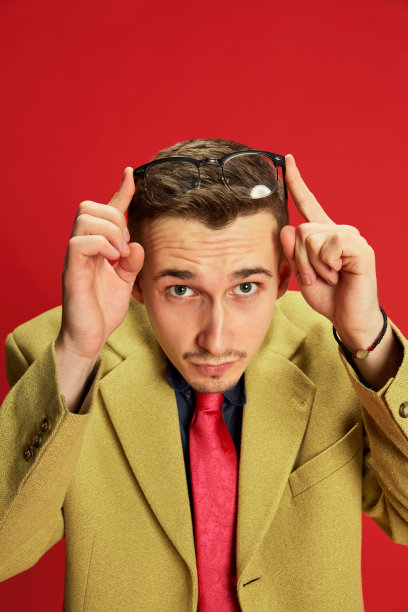 年轻男子的肖像在时尚的夹克和眼镜摆造型的红色背景。实习,工人。商业、情感、职业的概念图片下载