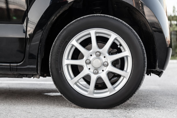 夏天黑色轮胎的机翼下的一辆黑色轿车特写与合金铝盘。汽车车间的季节性车轮更换。图片下载