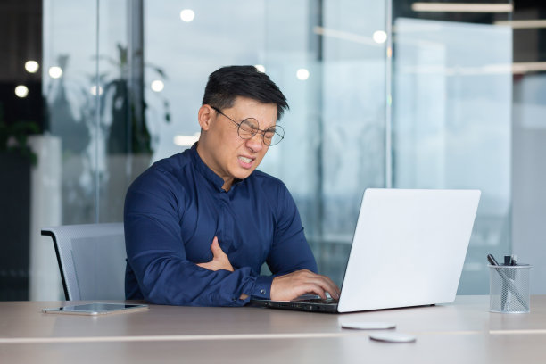 成熟的亚洲商人在办公室生病，男人心脏病发作，高级老板手牵着手胸口心痛，老板在办公室用笔记本电脑工作图片下载