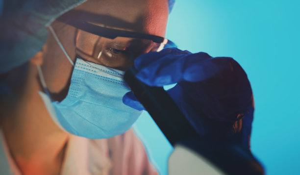 科学家戴着医用口罩在实验室用显微镜工作。图片下载