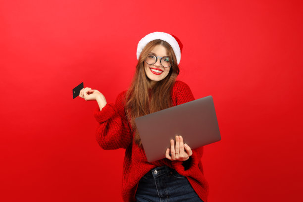 除夕夜网购。一名戴着圣诞老人帽、手里拿着笔记本电脑和支付卡的年轻女子正在网上购物和下单。图片下载