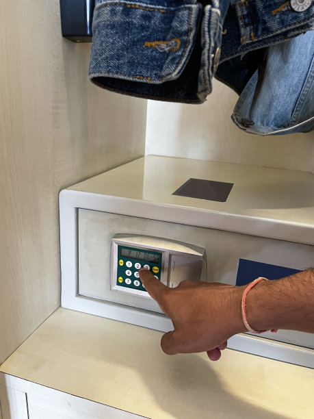照片中，一个无法识别的人正在使用酒店电子酒店衣柜保险箱上的键盘，打开保险箱存放贵重物品和钱，挂着牛仔夹克，焦点在前景图片下载