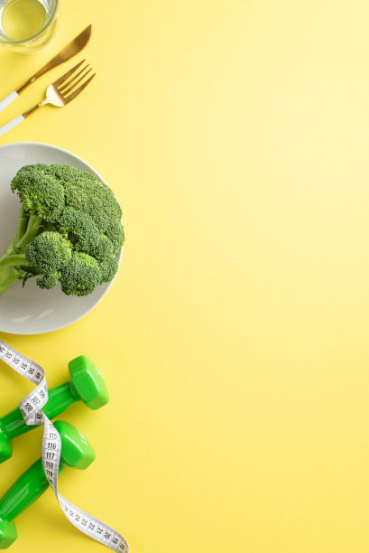 减肥的概念。俯视图垂直照片的盘子与花椰菜玻璃杯的水测量卷尺，餐具和哑铃在孤立的淡黄色背景与复制空间图片下载