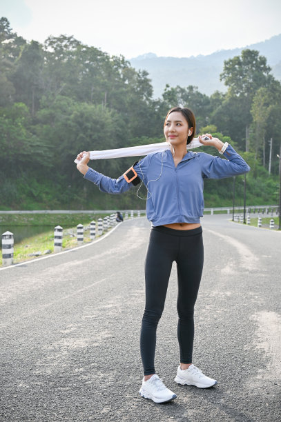 一个迷人的亚洲女人站在街上，拿着毛巾，戴着耳机听音乐。图片下载