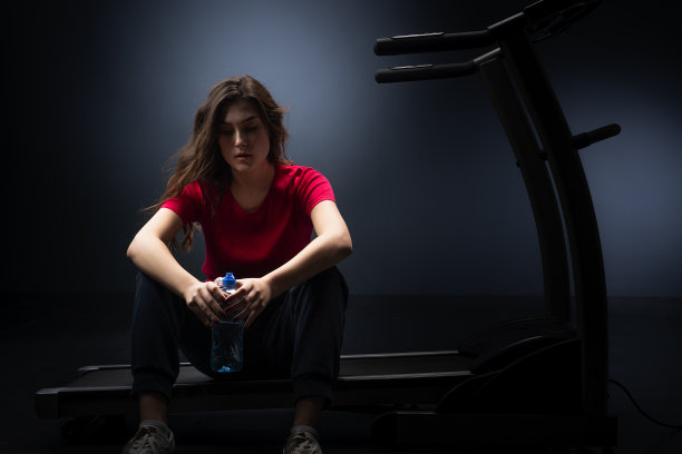疲惫的年轻女孩坐在健身房喝水。图片下载
