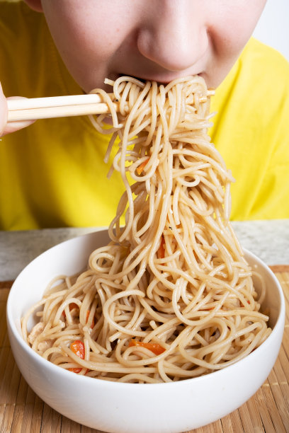 一个男孩用筷子吃日本面条和鸡肉和酱油。垂直方向图片下载