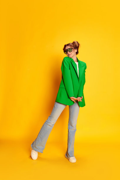 年轻可爱的女孩在明亮的绿色夹克的肖像在黄色的工作室背景。感觉害羞图片下载